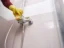 Person scrubbing soap scum off glossy bathroom shower tile with a sponge